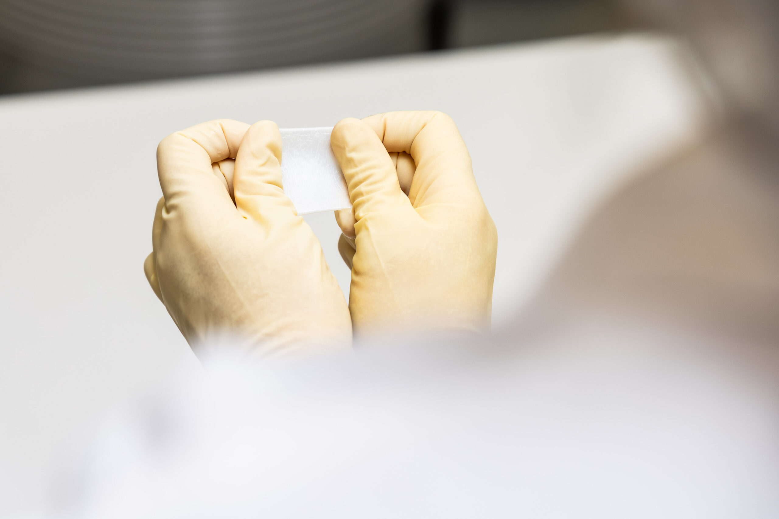 Gloved hands holding a small translucent Orthocell collagen membrane medical device in a sterile laboratory environment